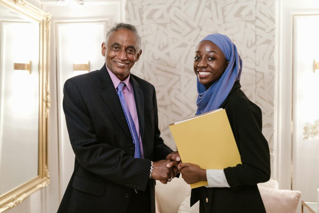 A business meeting with a friendly handshake between two adults in professional attire indoors.